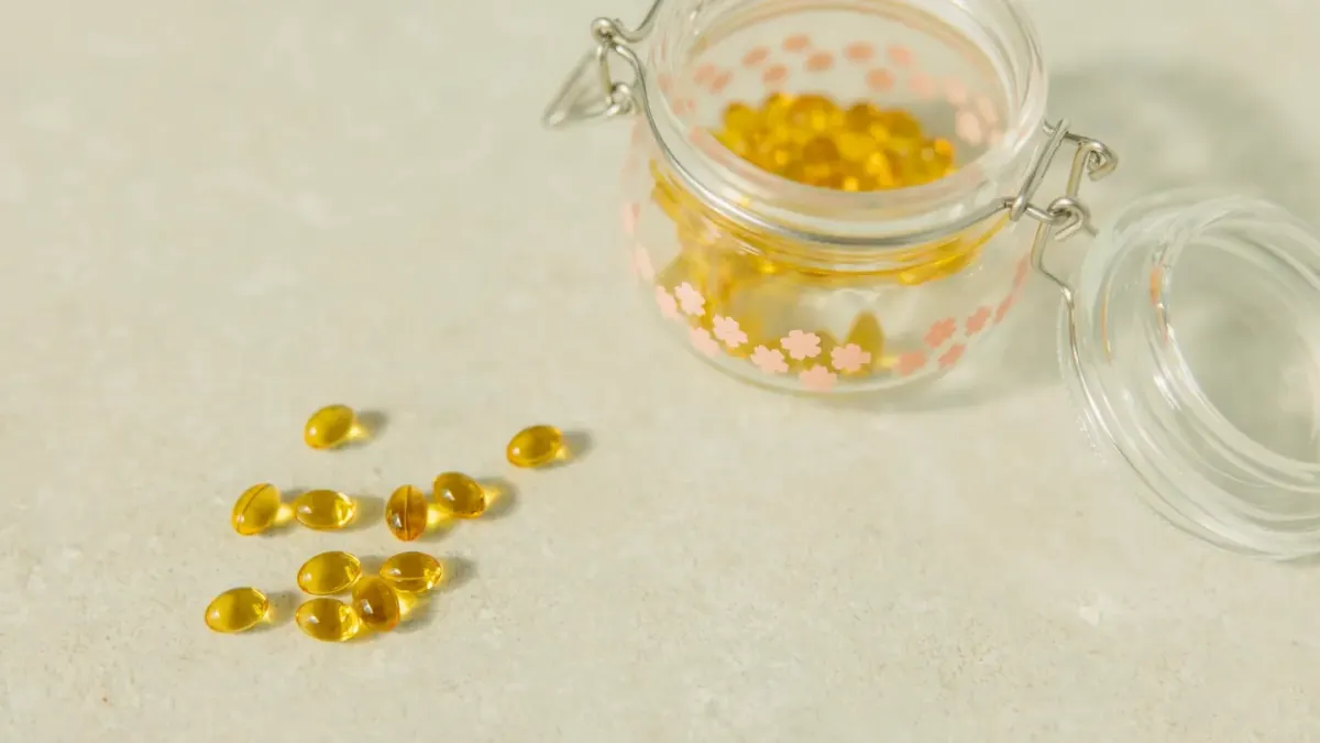 A dog owner opens a chewable supplement bottle on a kitchen counter while a dog waits nearby