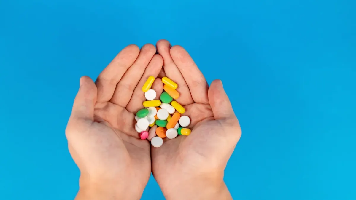 A dog owner's hand holding a soft chew, a capsule, and a small scoop of powder side by side