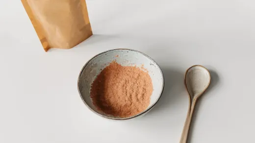 A measuring scoop of green-lipped mussel powder beside a dog's bowl