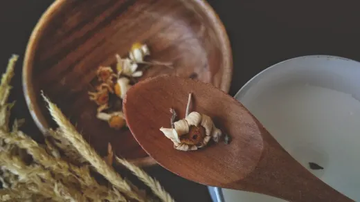 Dried chamomile flowers spilled beside a small ceramic bowl on a wooden kitchen table